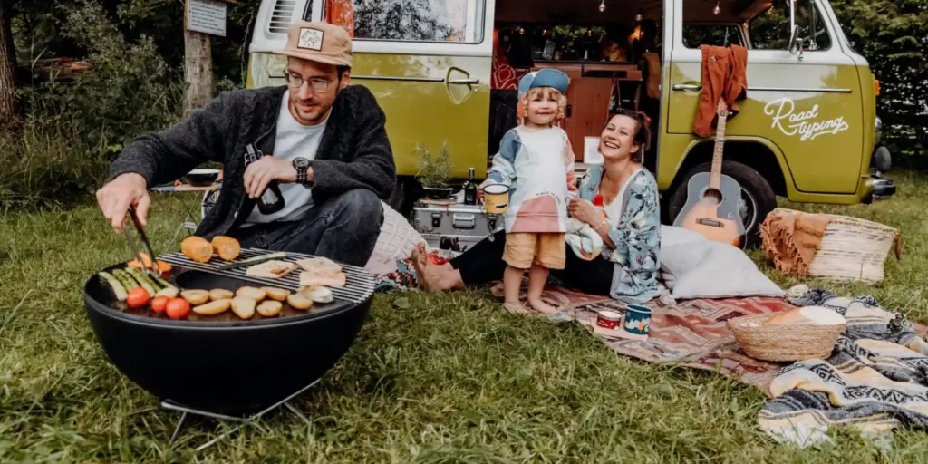 En familie er på campingtur og faren sitter og griller mat på Höfats Bowl bålpanne