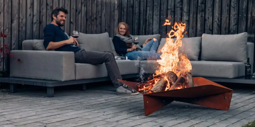 Et ektepar sitter utendørs på sofaen og ser inn i flammene på Höfats Triple bålpanne